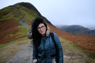 Portrait of smiling young woman standing on mountain against sky