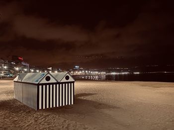 Illuminated lighting equipment on beach against sky at night