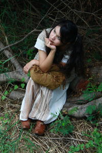 High angle view of woman looking away while sitting on tree branch