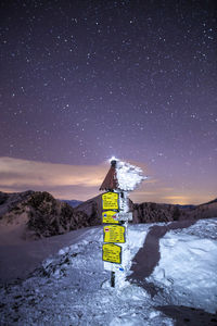 Information sign on snowcapped mountain against sky at night