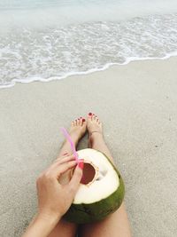 Low section of woman with coconut sitting at beach