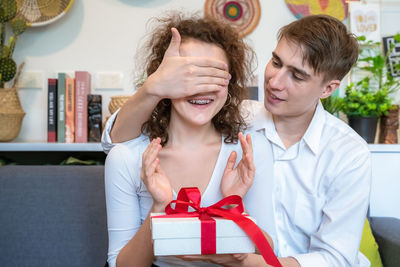 Man blind folding woman while holding gift