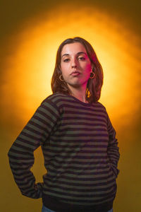 Portrait of young woman standing against yellow background