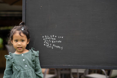 Portrait of cute girl writing alphabet on blackboard