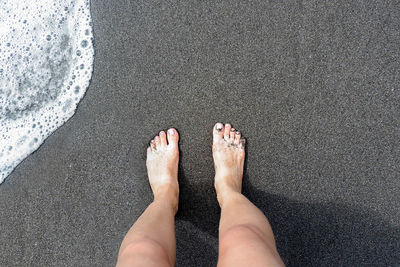 Low section of young woman standing on shore at beach