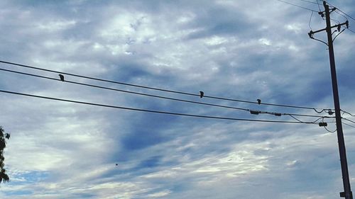 Low angle view of electricity pylon against cloudy sky