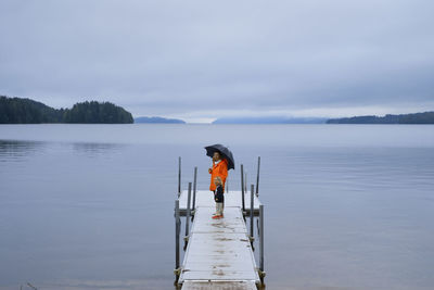 Rear view of man standing on pier over lake against sky