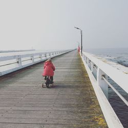 Rear view of man on pier at sea against clear sky