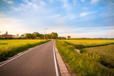 Empty road amidst field against sky