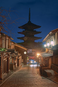 Illuminated street amidst buildings against sky at night