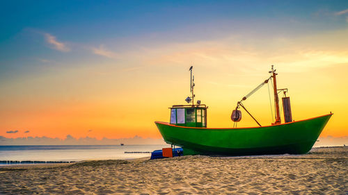 Ship moored on beach against sky during sunset