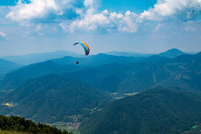 Person paragliding over mountain against sky