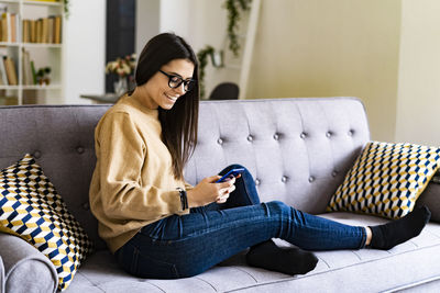 Young woman using mobile phone while sitting on sofa