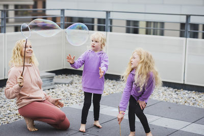 Smiling mother playing with bubble wand by daughters on rooftop