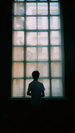 Silhouette boy looking through window