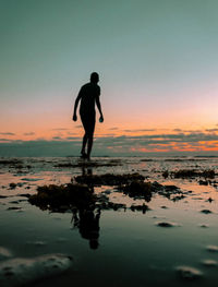 Silhouette man standing on beach against sky during sunset