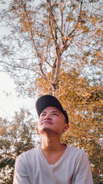 Portrait of young man looking away against trees