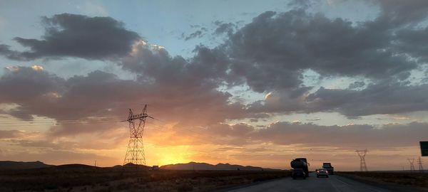 Vehicles on road against sky during sunset