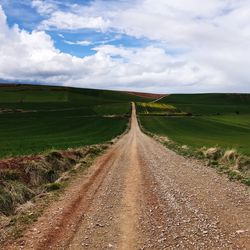 Dirt road amidst field against sky