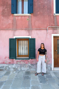 Full length portrait of smiling woman standing against building