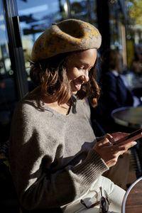 Smiling woman wearing beret using smart phone on sunny day
