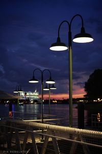 Illuminated street light by sea against sky at night