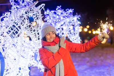 Portrait of smiling young woman with arms outstretched standing against wall