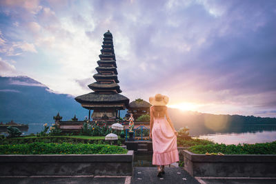 Woman standing at pura ulu danau temple against sky during sunrise