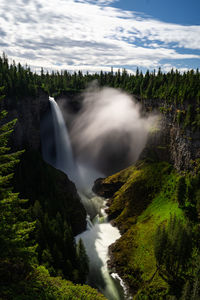 Scenic view of waterfall amidst trees against sky