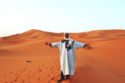 Full length of man with arms outstretched standing at desert against clear sky