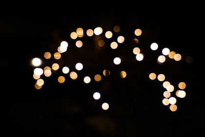 Defocused image of illuminated lights against sky at night