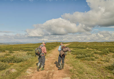 Rear view of men walking on field against sky