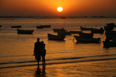 Rear view of silhouette couple standing in sea against sky during sunset