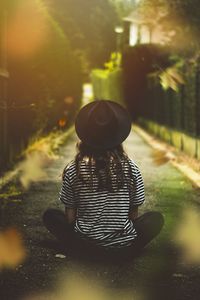 Rear view of woman sitting on footpath during sunny day