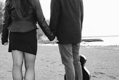 Midsection of man with guitar holding woman hand on beach