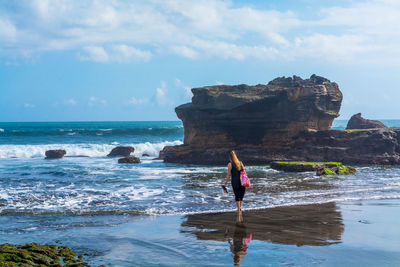 Rear view of woman walking on shore at beach against sky