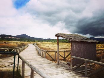 Wooden boardwalk amidst field against cloudy sky