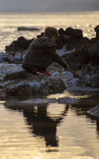 Man on rock at beach against sky during sunset