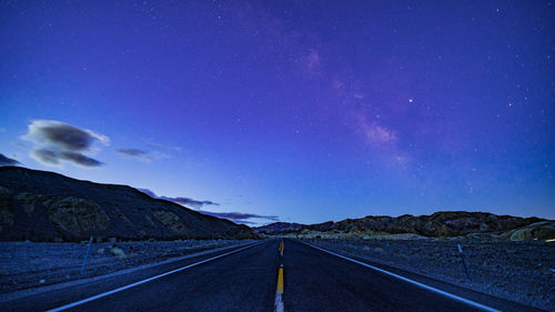 Empty road by mountain against sky at night