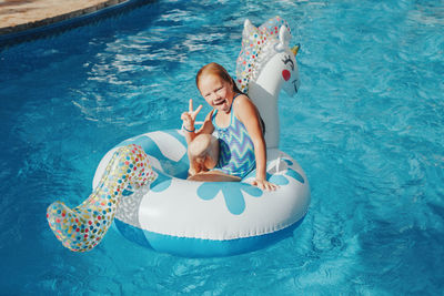 Smiling caucasian girl lying on inflatable ring unicorn. kid child having fun in swimming pool