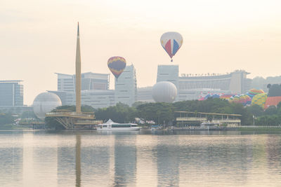 Hot air balloon flying over river with buildings in background