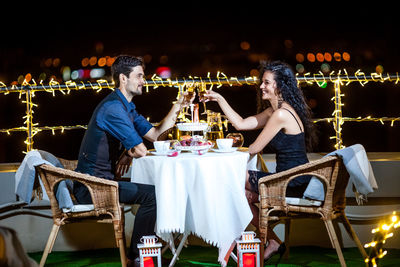 Couple toasting drinks on illuminated terrace at night
