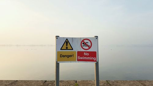 No swimming sign by sea against sky