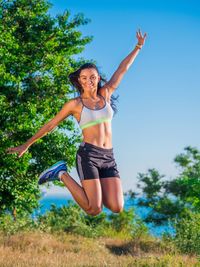 Happy young woman jumping against clear blue sky