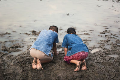 Rear view of siblings at barren land with water