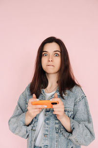 Portrait of a young woman in casual denim jacket with smartphone playing game, isolated on pink