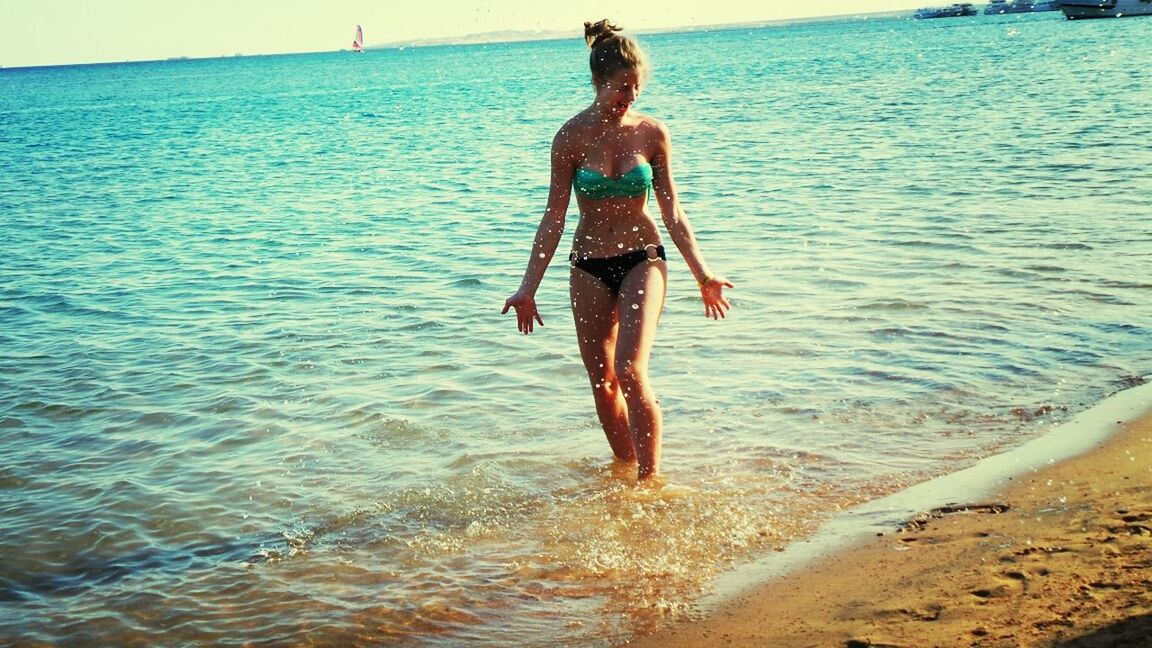 water, full length, sea, lifestyles, leisure activity, vacations, young adult, beach, person, casual clothing, enjoyment, shore, standing, bikini, fun, front view, young women, sand