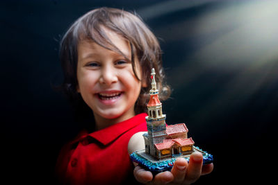 Portrait of smiling girl holding model house against black background