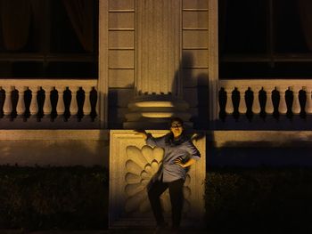 Woman standing by architectural column against concrete fence at night