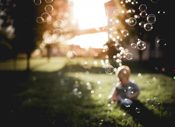 Baby boy playing at back yard with bubbles flying in foreground